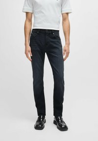 Dark blue denim jeans with a slim fit, featuring a standard five-pocket design and belt loops, paired with black loafers.