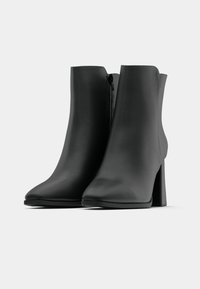 Μαύρες μπότες ankle από λείο υλικό, με μυτερή μύτη και παχιά τακούνι, διαθέτοντας φερμουάρ στο πλάι για κλείσιμο. Μεσαίο ύψος και κομψός σχεδιασμός.