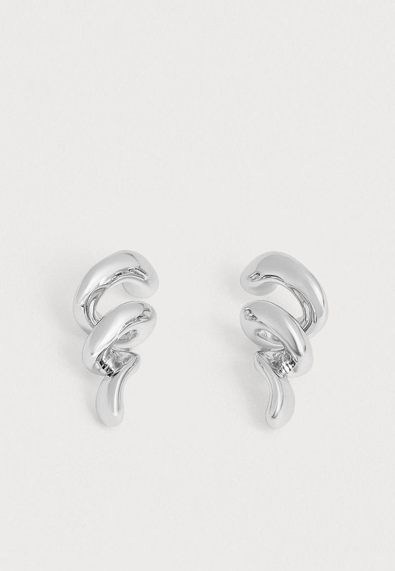Paire de boucles d’oreilles créoles en métal argenté brillant torsadé avec un design abstrait bouclé sur un fond blanc uni.