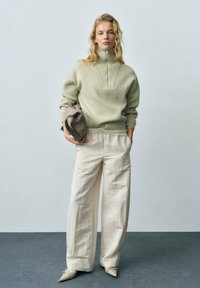 Light green knitted sweater with high collar and textured details, paired with loose cream trousers and pointed beige shoes.