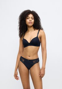 Conjunto de lingerie preta composto por um sutiã almofadado com alças ajustáveis e cuecas tipo biquíni com detalhes em renda. Tecido suave com textura lisa.