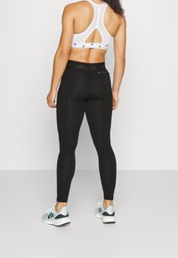 Leggings negras de cintura alta con textura suave, que cuentan con paneles laterales. Combinados con un sujetador deportivo blanco y zapatillas deportivas azul claro.
