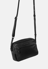 Schwarze Leder-Umhängetasche mit strukturierten Oberflächen, einer Vorderreißverschlusstasche und einem verstellbaren Trageriemen. Rechteckige Form mit minimalem Zubehör.