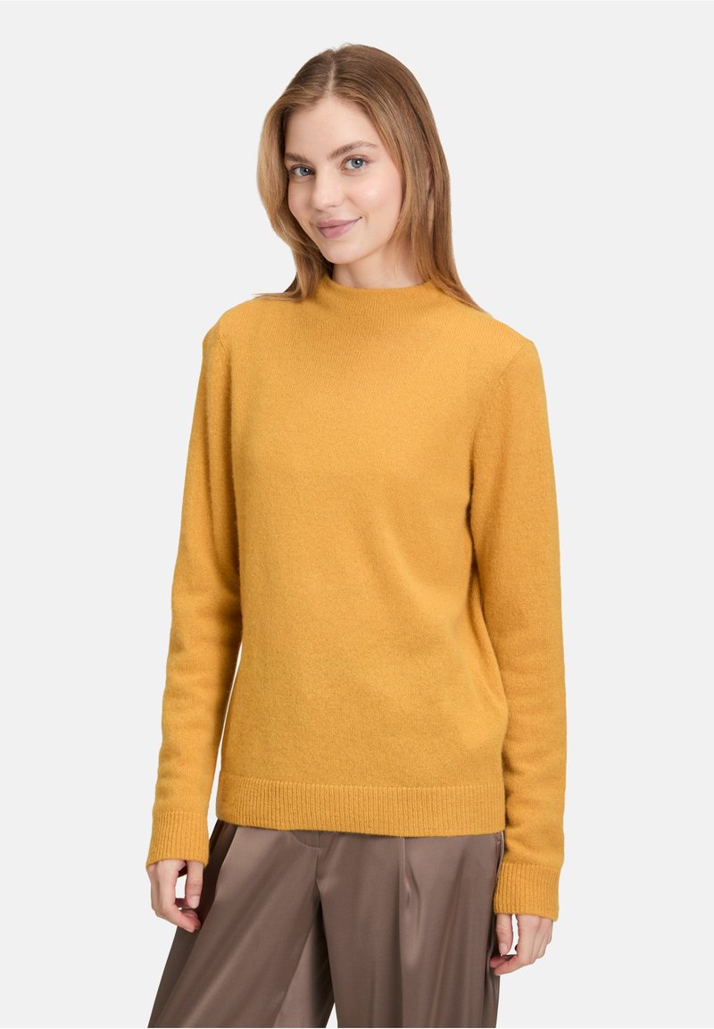 Pull jaune moutarde à manches longues, décolleté rond et ourlet côtelé. Fabriqué en tissu en maille douce, il présente une coupe décontractée.