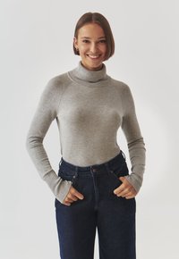 Maglione grigio a collo alto con maniche lunghe, realizzato in un morbido tessuto a maglia, abbinato a jeans in denim scuri a vita alta.