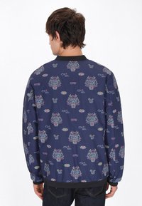 Giacca bomber navy con un motivo geometrico che presenta volti colorati, piante e occhiali da sole. Collo nero e polsini e orlo elastici.