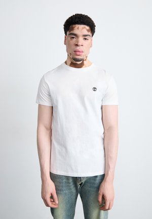 White cotton t-shirt with short sleeves, crew neck, and small black tree logo on the upper left chest. Worn with blue jeans.