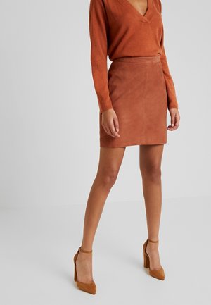 Woman wearing a rust-colored V-neck sweater, matching suede mini skirt, and tan high-heeled ankle-strap shoes against a plain background.