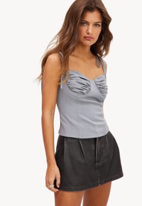 Lichtgrijze getailleerde top met een sweetheart halslijn, voorzien van een geplooide textuur en dunne bandjes, gecombineerd met een zwarte leren minirok.