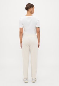 Top bianco a maniche corte con scollo rotondo, abbinato a pantaloni della tuta beige chiaro e morbidi con vita elastica e tasche laterali.
