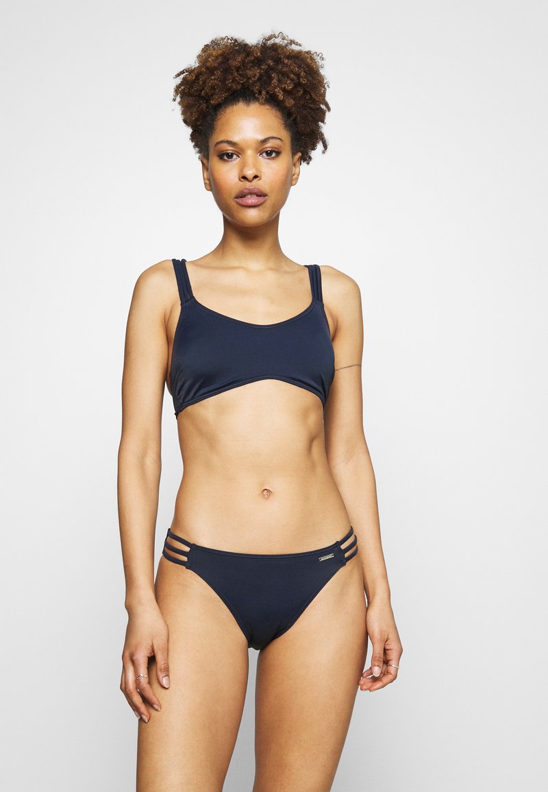 Navy blue bikini set made of smooth fabric; top has wide straps and a simple design. Bottom features double side cutouts for accents.