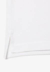 Tissu en coton blanc avec un tissage texturé, doté d'un bord replié et d'une petite fente sur le côté pour faciliter les mouvements.