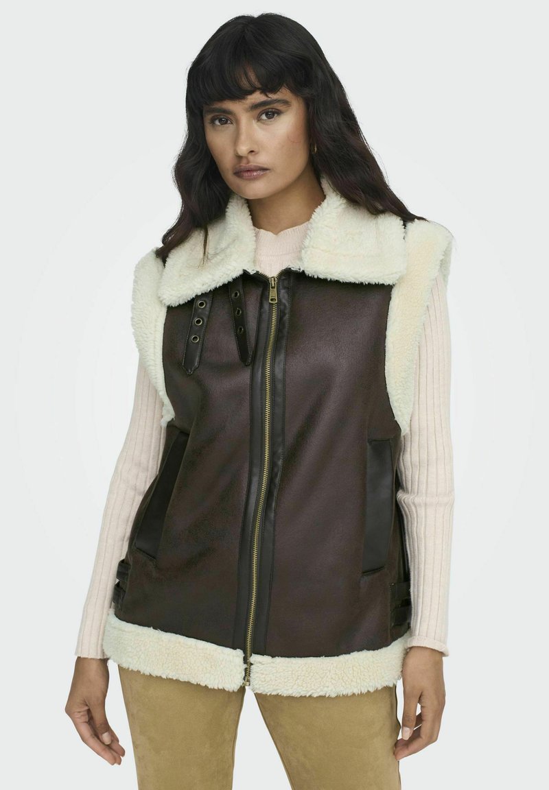 Bruine nepleren vest met een crèmekleurige nep-shearling kraag en zoom, frontale ritssluiting en zijzakken, met verstelbare details aan de zijkanten.