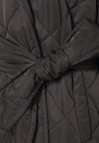 Tissu noir matelassé noué en un large nœud avec des coutures diagonales visibles et une texture rembourrée.