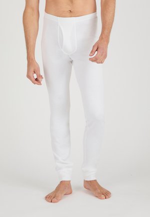 Hombre con pantalones largos interiores blancos lisos, de pie descalzo contra un fondo blanco.