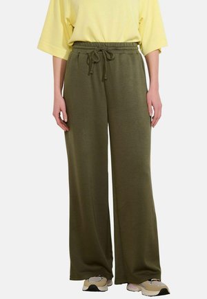 Luźne oliwkowo-zielone spodnie z troczkiem w talii, noszone z beżowo-białymi trampkami i żółtą bluzką z krótkim rękawem.