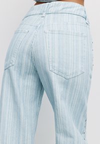 Jeans a gamba larga, a righe azzurro chiaro, con vita alta, tasche posteriori e dettagli in bottone sui lati. Realizzati in tessuto denim.