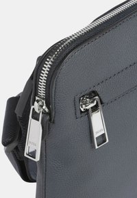 Borsa in pelle grigia con finitura testurizzata, dotata di una cerniera argentata, due linguette e una tracolla in tessuto. Design semplice e rettangolare.