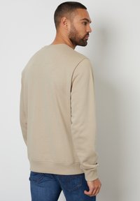 Sudadera de algodón beige con mangas largas y cuello redondo, que presenta puños y dobladillo acanalados, textura suave y un ajuste relajado.