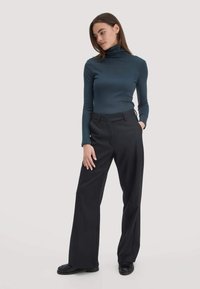 Diep teal coltrui gecombineerd met zwarte, hoge taille, wijdvallende broeken. Soepele textuur en een op maat gemaakte stijl met een strakke pasvorm.
