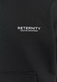 Czarna bluza z teksturowanej tkaniny z kieszenią kangurką. Z przodu widoczny jest biały napis: "RETERNITY CREATIVE DEPARTMENT."
