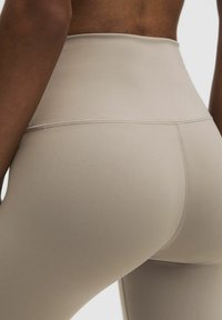 Beige high-waisted leggings van rekbare stof, met een gladde textuur, voorzien van platte naden en een aansluitend ontwerp dat de heupen accentueert.