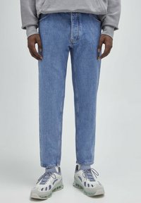 Jeans in denim azzurro chiaro con taglio dritto, cinque tasche e dettagli di cucitura sottili, abbinati a sneaker grigie.