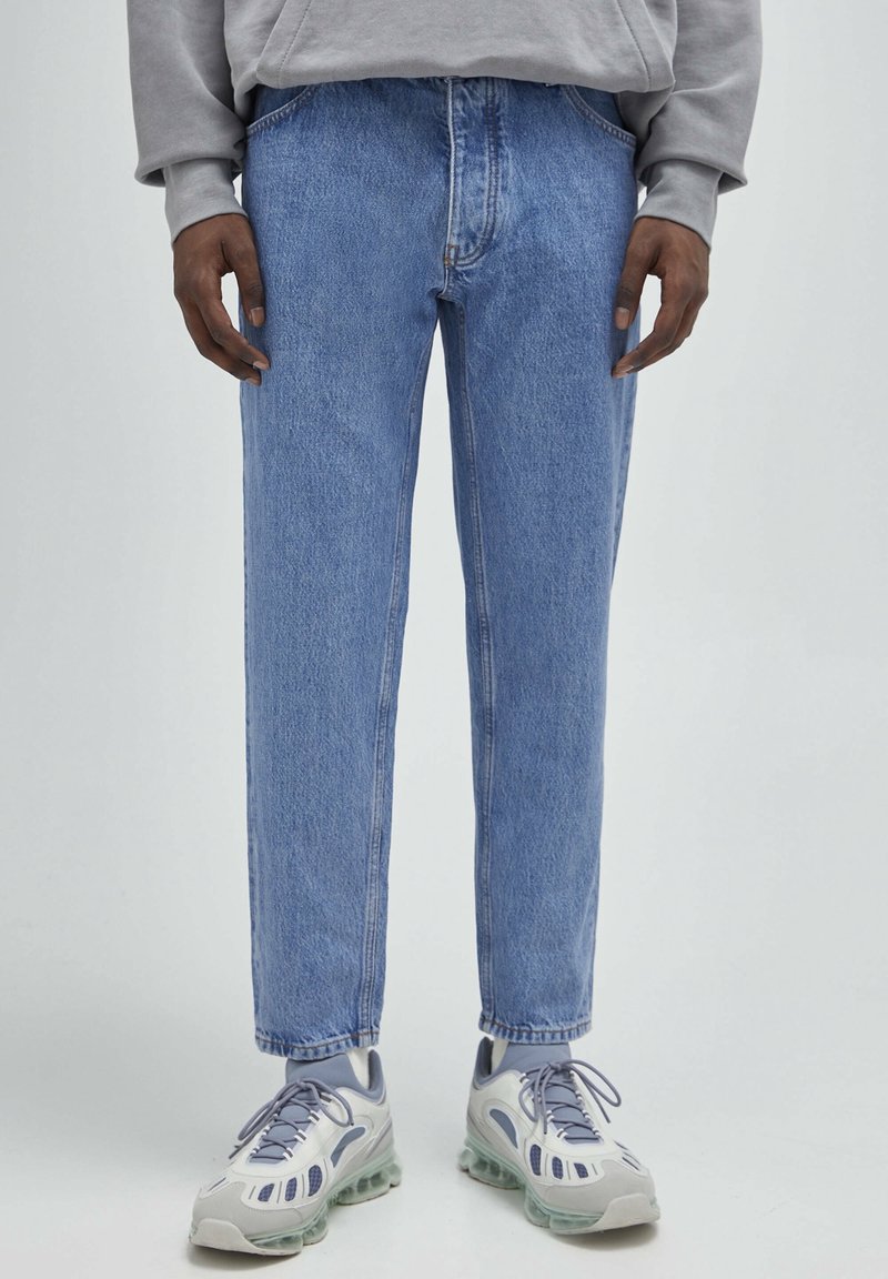 Jeans in denim azzurro chiaro con taglio dritto, cinque tasche e dettagli di cucitura sottili, abbinati a sneaker grigie.