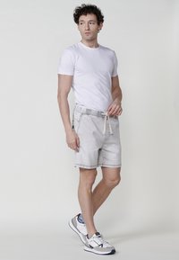 Pantalones cortos de mezclilla gris claro con cintura elástica y cordón. Combinados con una camiseta blanca ajustada y zapatillas deportivas blancas con acentos azules.