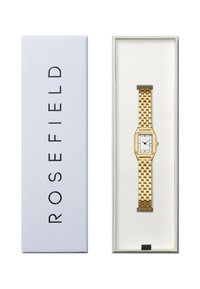 Reloj hexagonal dorado con una esfera blanca y manecillas negras, con una pulsera de malla. Presentado en una caja azul claro con texto negro.