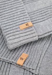 Sciarpa grigia lavorata a maglia con trama a coste, con un'etichetta in pelle marrone impressa con la lettera "W". Dettagli includono una finitura pulita.