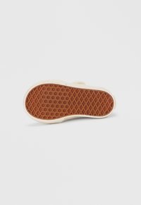 Semelle de chaussure en caoutchouc avec un motif texturé en nid d'abeille brun, bordée d'un matériau de couleur crème. Forme plate et arrondie.