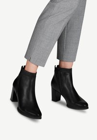 Schwarze Leder-Stiefeletten mit spitzem Kopf, Blockabsatz und seitlichem Reißverschluss. Der obere Teil hat ein strukturiertes, elastisches Panel für Flexibilität.