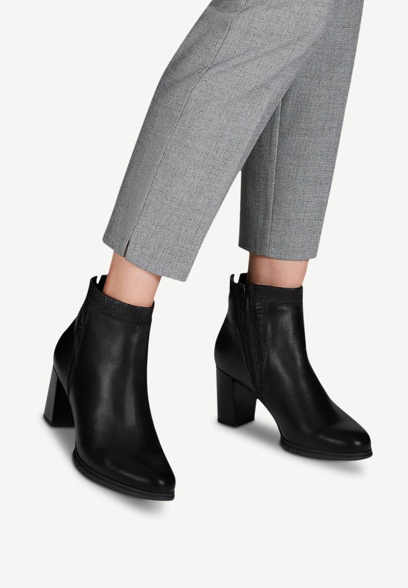 Schwarze Leder-Stiefeletten mit spitzem Kopf, Blockabsatz und seitlichem Reißverschluss. Der obere Teil hat ein strukturiertes, elastisches Panel für Flexibilität.