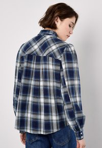 Navy and white plaid shirt with long sleeves, featuring a yoke detail on the back and button cuffs. Cotton fabric with a smooth texture.