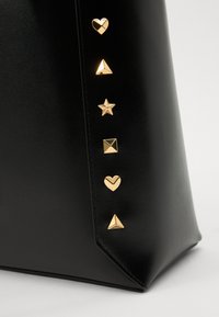 Borsa a tracolla in pelle nera con accessori decorativi in tonalità oro, caratterizzata da cuori, stelle e forme geometriche su un lato.