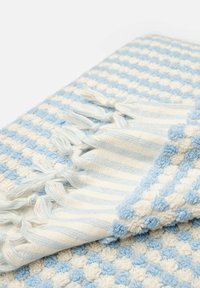 Manta tejida texturizada en azul claro y crema. Presenta un patrón de lunares y bordes a rayas con borlas para un detalle adicional.