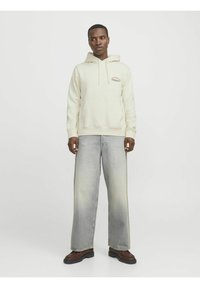 Krämfärgad hoodie med känguruficka och tryckt detalj; ihop med vida ljustvättade jeans och bruna stövlar. Enkel, avslappnad design.