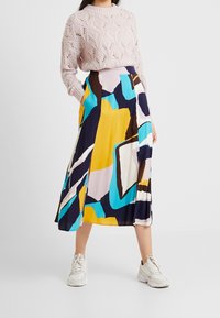Maglione rosa a maglia con un motivo a rombi, abbinato a una gonna midi fluida multicolore con forme geometriche audaci in giallo, blu e marrone.