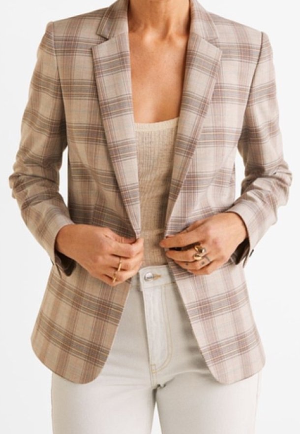 Blazer à carreaux beige, doté d'épaules structurées et d'une fermeture à un bouton. Porté sur un haut côtelé et associé à un jean blanc.
