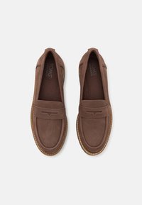 Zapatos marrones tipo slip-on con un acabado de ante suave, punta redonda, cuello acolchado y un diseño decorativo de costura en la parte superior. Suela de goma.