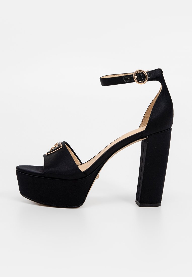 Sandales à plateforme en satin noir avec un large talon, bout ouvert et bride de cheville présentant une boucle en métal doré et un accent décoratif sur le devant.
