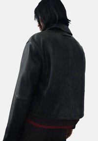 Black leather jacket with a fitted silhouette, textured finish, and a simple collar. Features a mid-length cut and subtle stitching details.