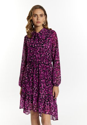 Abito rosa con stampa leopardata, maniche lunghe e un fiocco al colletto. Presenta un orlo arricciato e un tessuto leggero.