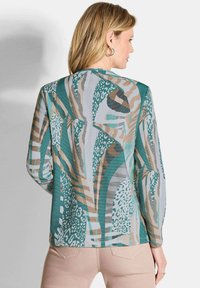 Langärmlige Bluse mit einem grünen, beigen und blauen abstrakten Muster, aus leichtem Stoff mit strukturierter Oberfläche.