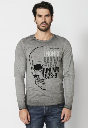 Hosszú ujjú szürke póló, fekete koponya grafikával és szöveges elemekkel, kerek nyakkivágással és puha tapintással.