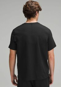 Tricou negru cu manșon scurt, dotat cu guler rotund, dintr-un material moale și cu un design simplu. Cusăturile vizibile de-a lungul gâtului din spate adaugă detaliu.