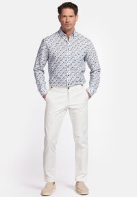 Witte button-down shirt met een blauw en bruin bloemenpatroon, gecombineerd met witte broek. De outfit heeft een ontspannen pasvorm en zachte stof.