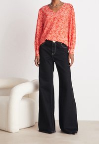 Rot gemusterte V-Ausschnitt-Bluse mit floraler Motivreihenfolge, kombiniert mit hoch taillierten, schwarzen, weit geschnittenen Hosen, die über Kontrastnähte und eine silberne Hardware-Akzent verfügen.