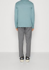 Světle modrý top s dlouhým rukávem, šedé kalhoty a tenisky v různých barvách. Hladký materiál, volný střih a minimalistické designové detaily.